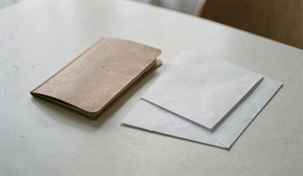 Un carnet fermé et une enveloppe vierge reposent sur une table claire, sans nom ni adresse visible dans la scène.